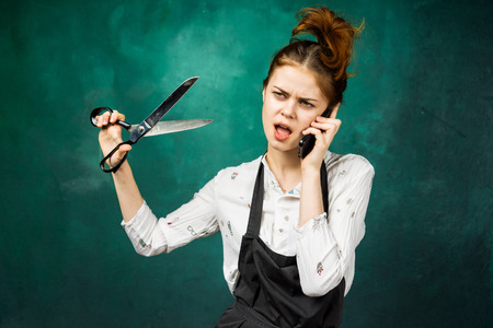 angry nervous young girl holding big scissors in her hand and talking on the phoneの写真素材