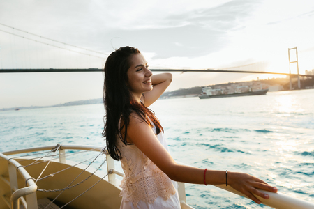 A young girl traveler relaxes during a yacht cruise, straightens her hair, enjoys the sunsetの写真素材