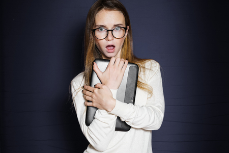 a frightened girl with glasses pressed her tablet to her and looks at the camera, isolatedの写真素材