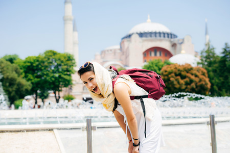 A young woman in a scarf with a backpack on the background of Aya Sofia and a fountain laughing. Summer vacation, travelerの写真素材