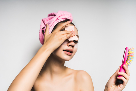 Young beautiful girl with a pink towel on her head cleans the face, holds in her hand a pink combの写真素材