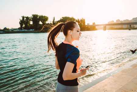Sports girl with phone in hands runs at sunsetの写真素材