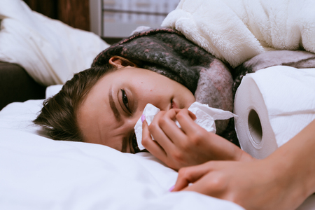 sad young girl gets sick, sneezes, sore throat, neck warm scarf, feels badの写真素材