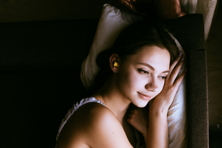 an attractive young girl went to bed, sleepily looks out the window, and her ears earplugs