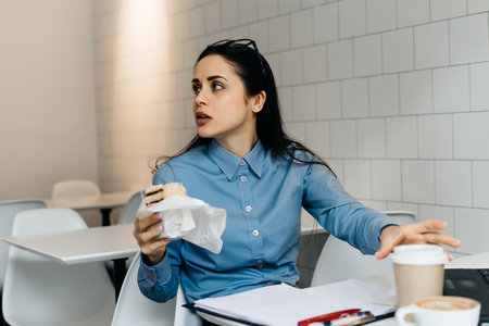busy business woman in a blue shirt working in a cafe with a laptop, and having breakfastの写真素材