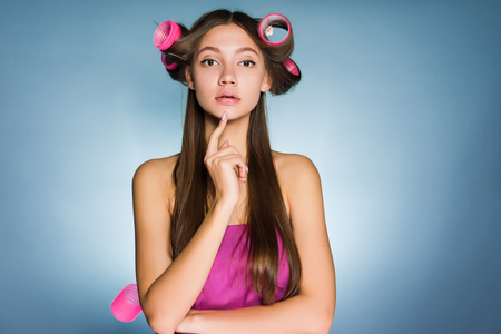 a beautiful girl thinks of a fashionable hairstyle, on her head big curlersの写真素材