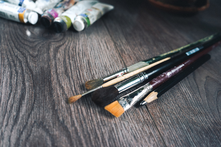 on a wooden surface lie tubes with oil paint and artistic brushes of different sizes