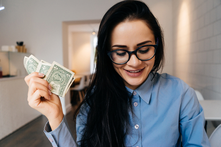 business happy business woman with glasses holds money in her hands, thinks about businessの写真素材