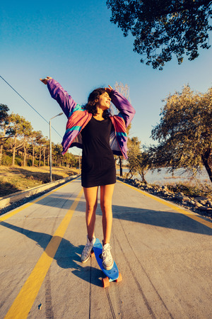 stylish young girl in a fashionable purple jacket skating, enjoying the good weatherの写真素材