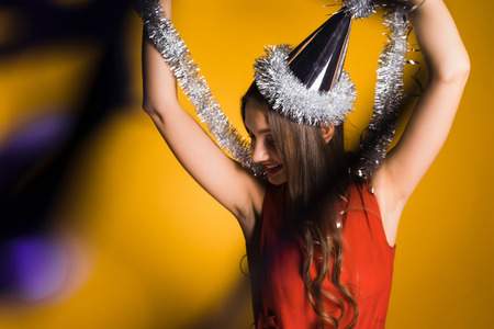happy young girl celebrates the new year and christmas in a festive cap, holds a silver tinselの写真素材