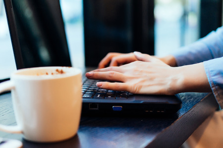 girl freelancer working in a cafe for a laptop, next to a mug with fragrant coffeeの写真素材