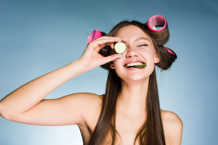 happy young girl takes care of herself, on the head of the curler, keeps the cucumber for moisturizing the skin of the faceの写真素材