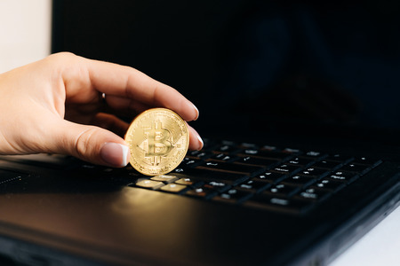 girl financier holds in her hand a gold bitcoin on a laptop backgroundの写真素材