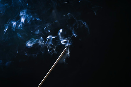 on a dark background a lighted fragrant stick, blue smokeの写真素材