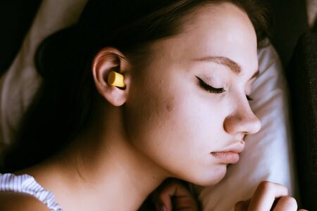 beautiful young girl sleeping, in ear-earplugs against noiseの写真素材