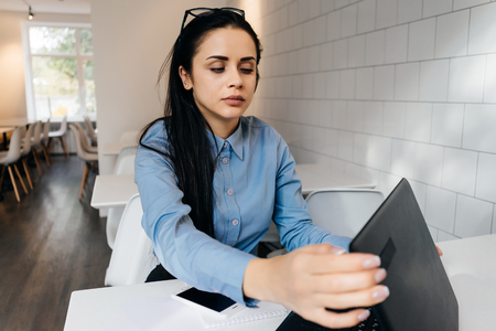 tired young girl student in blue shirt working on laptop in cafeの写真素材