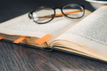on a wooden surface is a book with bookmarks, glasses in black rimの写真素材