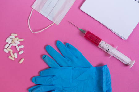 on a pink surface are blue gloves, tablets, a syringe and a notebookの写真素材