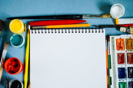 on a blue table lie art supplies, drawing paper, watercolors and gouache, brushesの写真素材