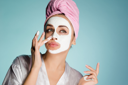 young cute girl with a pink towel on her head puts a white nutritious mask on her faceの写真素材