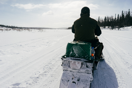 in the far cold north, a man in warm clothes rides a snowmobile through a snow-covered fieldの写真素材