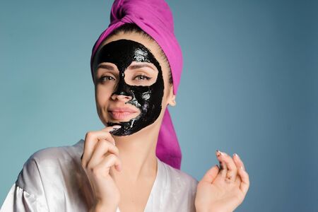 smiling young girl wants clean skin on her face, has put a black mask against black dotsの写真素材