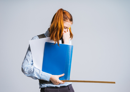 tired tired sad red-haired schoolgirl holds in hands educational documents and a rulerの写真素材