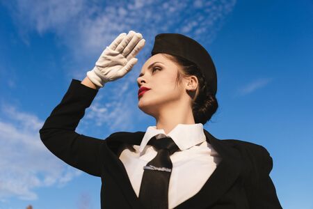 confident young girl stewardess looks into the distance, against the blue sky
