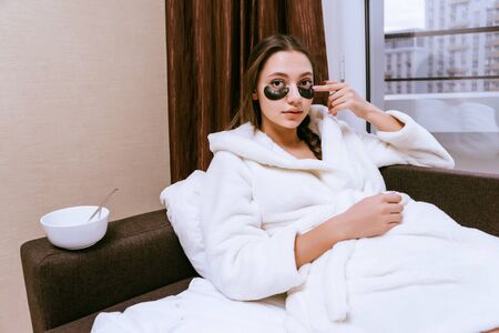 a young girl just woke up, sits in bed, under the eyes of black silicone patches, next to a plate with breakfast cerealの写真素材