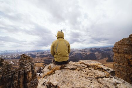a man sits on the edge of a cliff and looks at the mountains, enjoys natureの写真素材