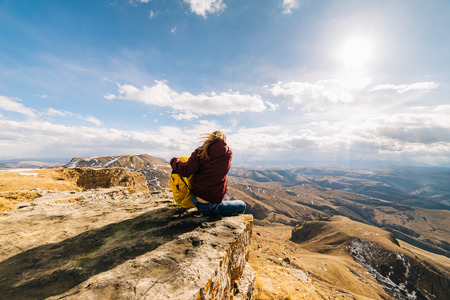 a young girl sits on the edge of a mountain, travels along the Caucasian ridge with a backpack