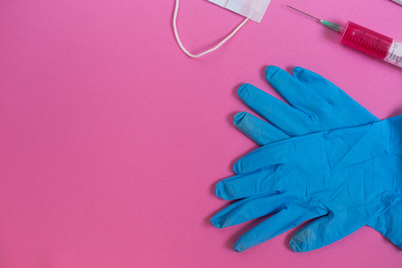 on a pink surface there are blue medical gloves and a syringe