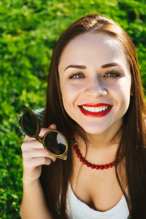 Smiling woman shows sunglasses, demonstrate glasses against the green lawnの写真素材