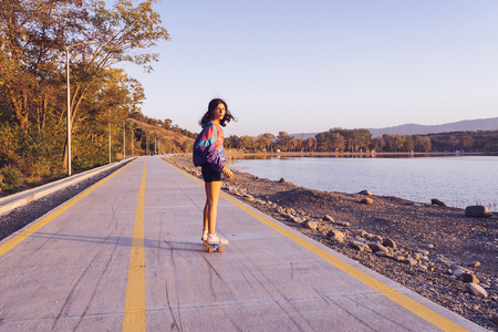 stylish young girl is riding a longboard on the road in the sunの写真素材