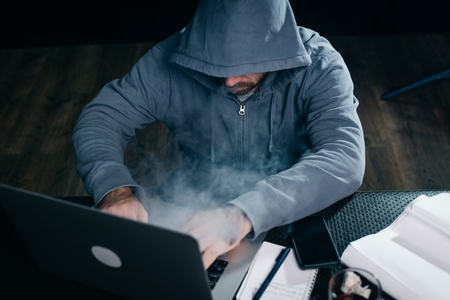 mysterious man in a hood doing something illegal on a laptop, smokingの写真素材