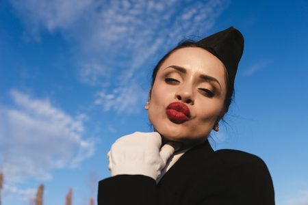 funny young woman stewardess sends an air kiss against the blue skyの写真素材