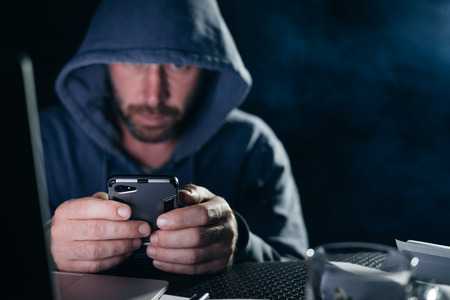 dangerous mysterious bearded man hacks smartphone, hides his face under the hoodの写真素材