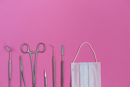 on the pink surface are medical dental instruments and a white mask