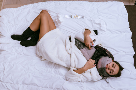 young sad girl lies in bed all day, gets sick, sore throat and headの写真素材