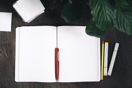 on a wooden floor lies a notebook with clean white sheets and a red pen,