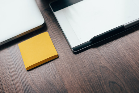 on a wooden surface lie a graphic tablet and yellow paper