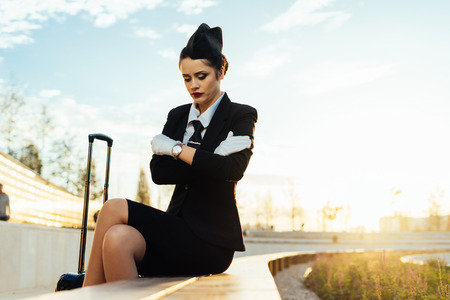 confident slender woman stewardess in uniform sits in the park, waiting for the flight, frozeの写真素材