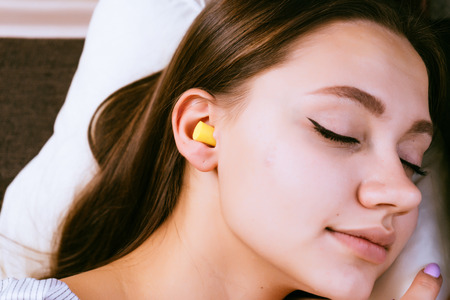 cute young girl sleeping in bed, in the ears yellow earplugs against street noiseの写真素材