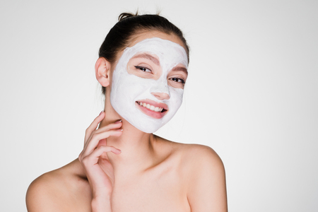 a funny smiling girl has put on the face a white nutritious mask against wrinklesの写真素材