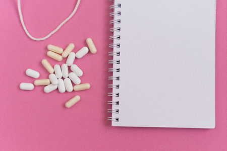 on a pink surface is a white notebook and tabletsの写真素材