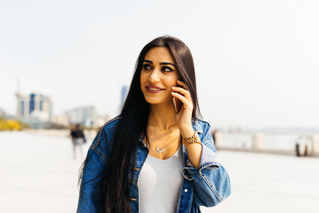 young girl walking in sunny city talking on the phone smilingの写真素材