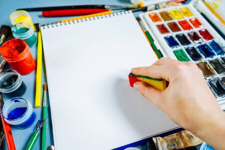 woman painter draws on white paper, beside lies a colorful gouache and watercolorsの写真素材