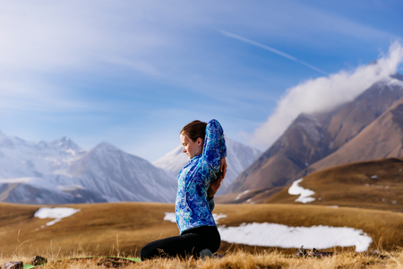 active young girl in a blue jacket doing yoga in the background of the Caucasian mountainsの写真素材