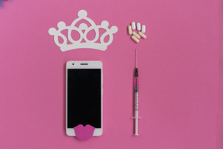 a beautifully decorated phone lies next to a prepared syringeの写真素材