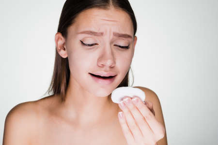 sad young woman holding a cotton disc for skin cleansingの写真素材